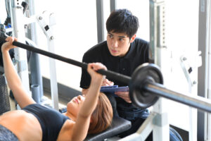 男性トレーナーが女性の筋力トレーニングを補助している写真